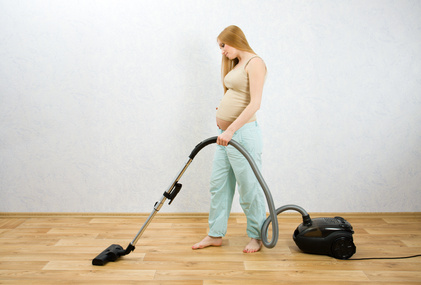 Pregnant woman cleaning floor with vacuum cleaner
