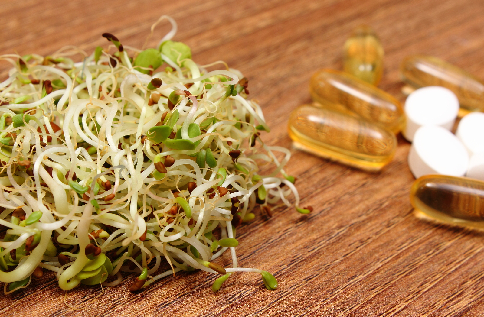 Alfalfa and radish sprouts with tablets supplements on wooden surface, choice between healthy eating and pills, healthy lifestyle food and nutrition